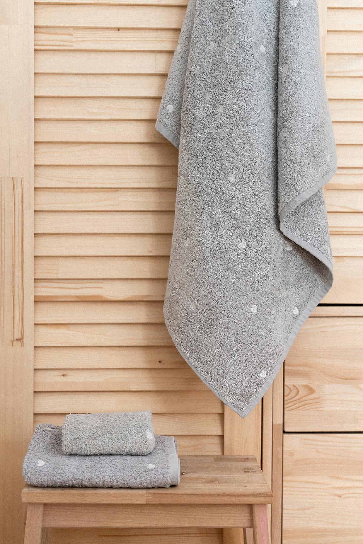 Toalla de baño gris de calidad con estampado de corazones blancos, exhibida sobre un suelo de madera