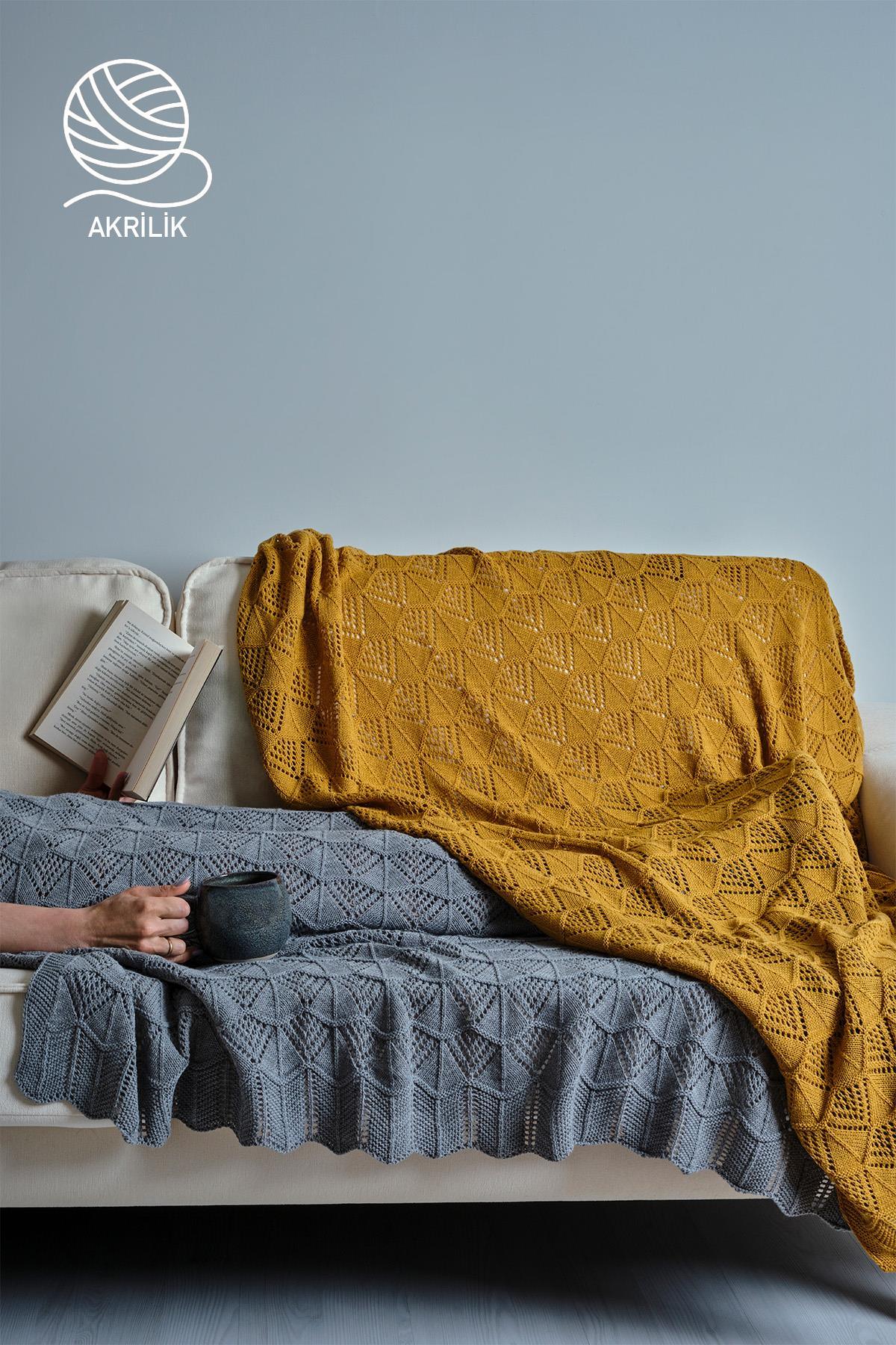 Manta de TV de punto acrílico con estampado en tonos amarillo y gris, extendida sobre un sofá.