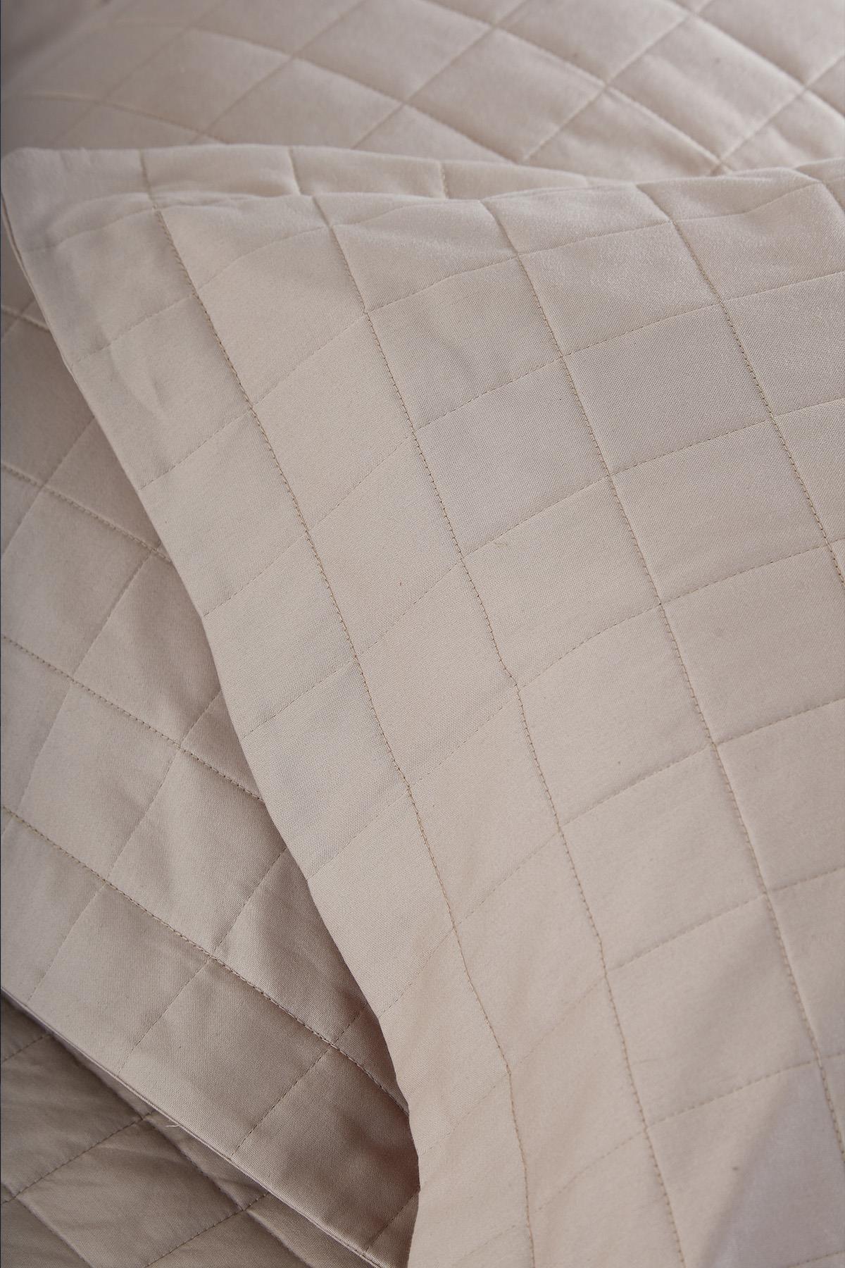 Primer plano de colcha acolchada beige para cama doble con funda de almohada