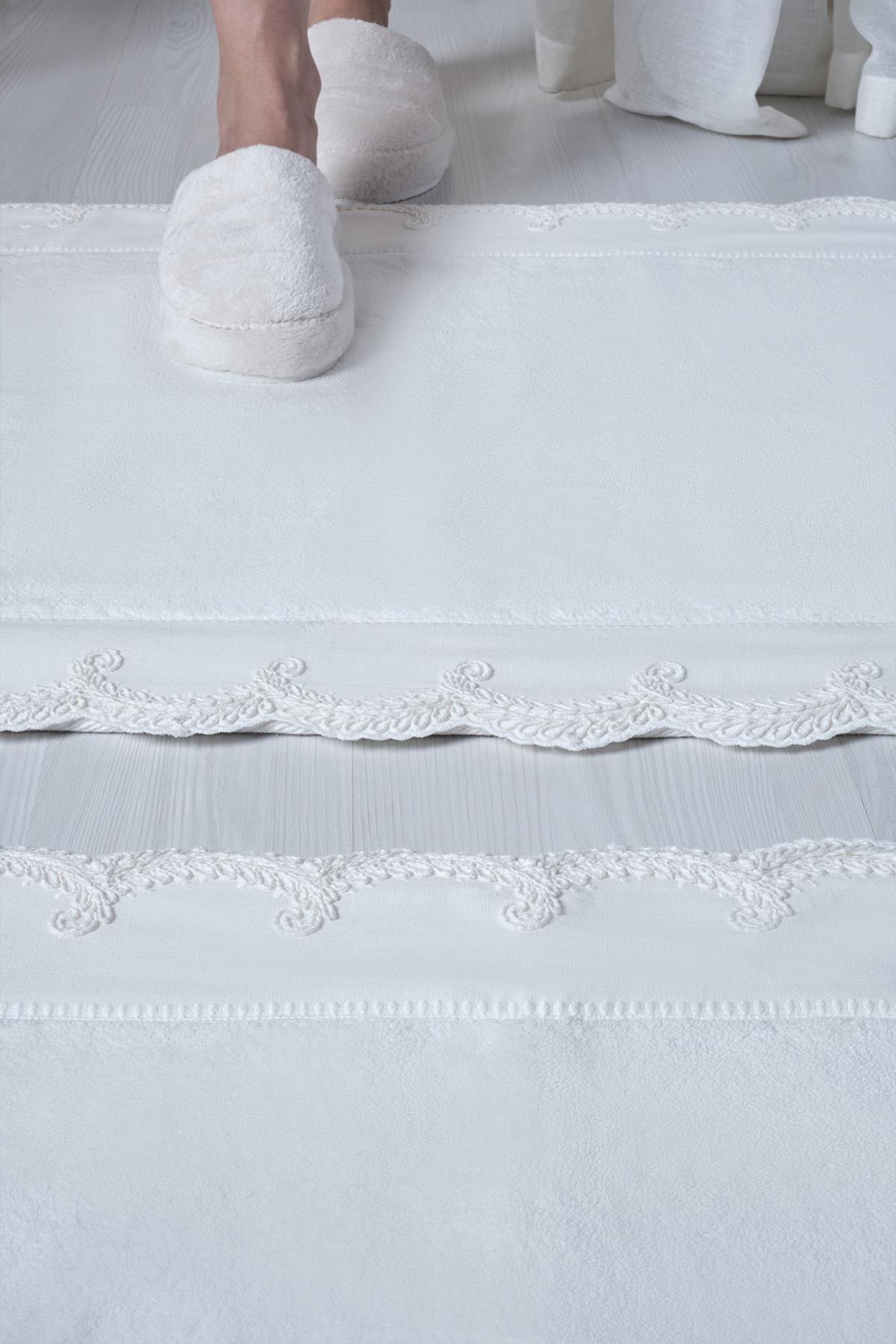 Juego de 2 alfombrillas de baño blancas con bordados y detalles de encaje en los bordes, sobre un suelo moderno