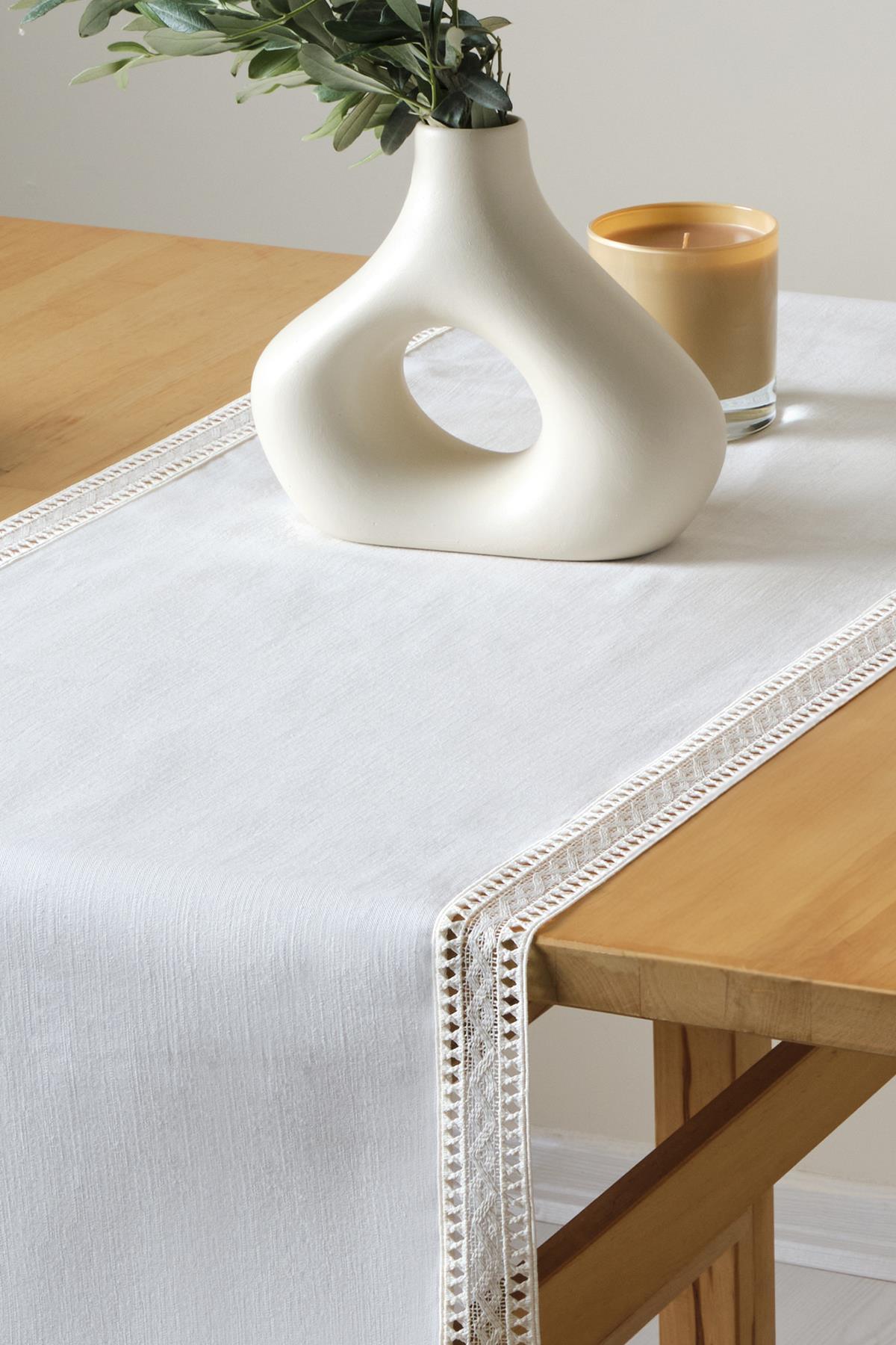 Camino de mesa blanco con encaje, presentación decorativa con jarrón moderno y vela sobre mesa de madera