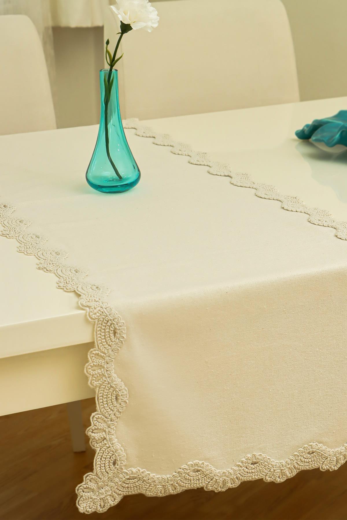 Camino de mesa color crema con detalles de encaje, sobre una mesa de comedor moderna con un jarrón decorativo