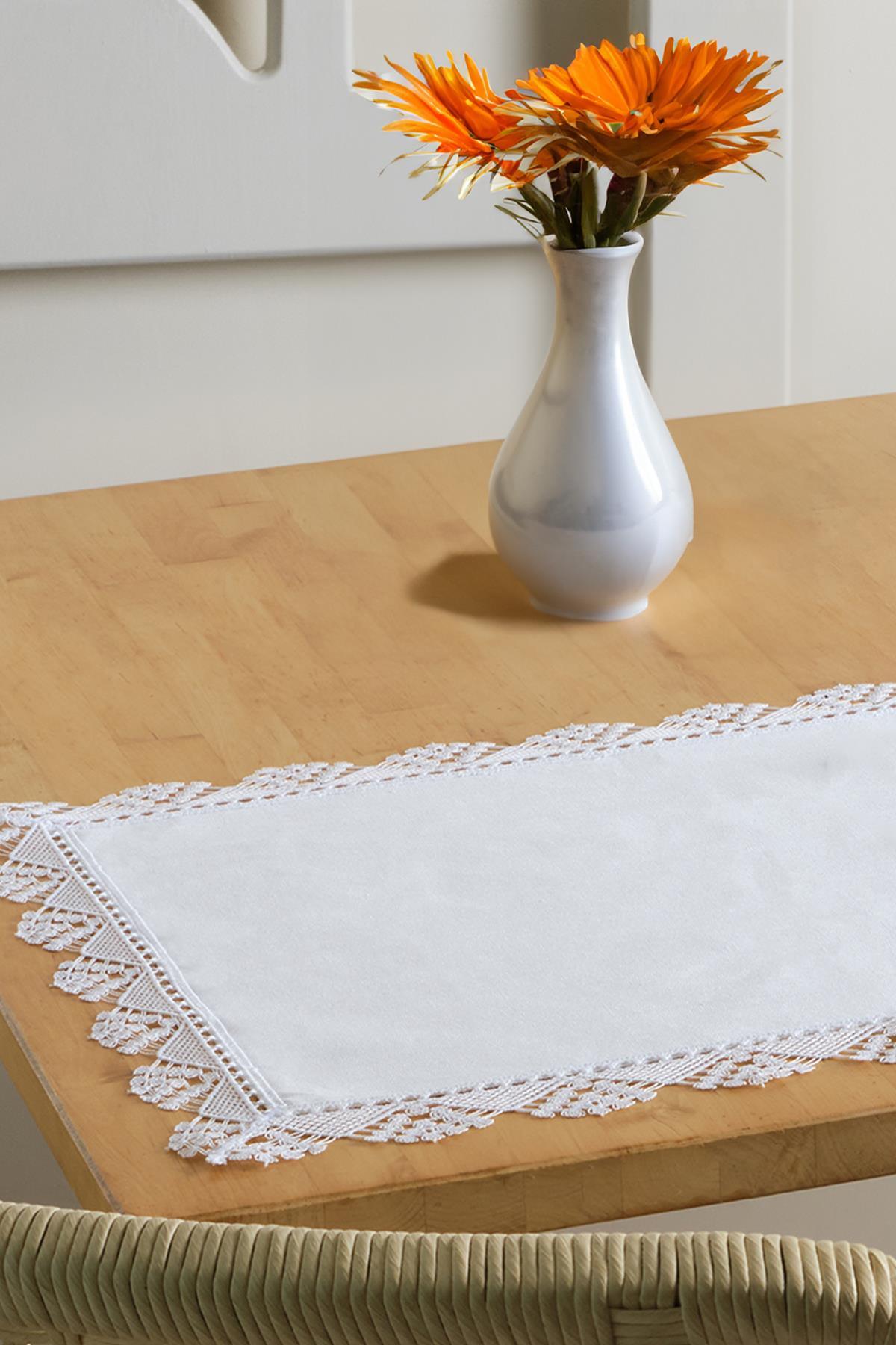 Camino de mesa blanco con borde de encaje y mantel individual, sobre una mesa de madera con un jarrón decorativo