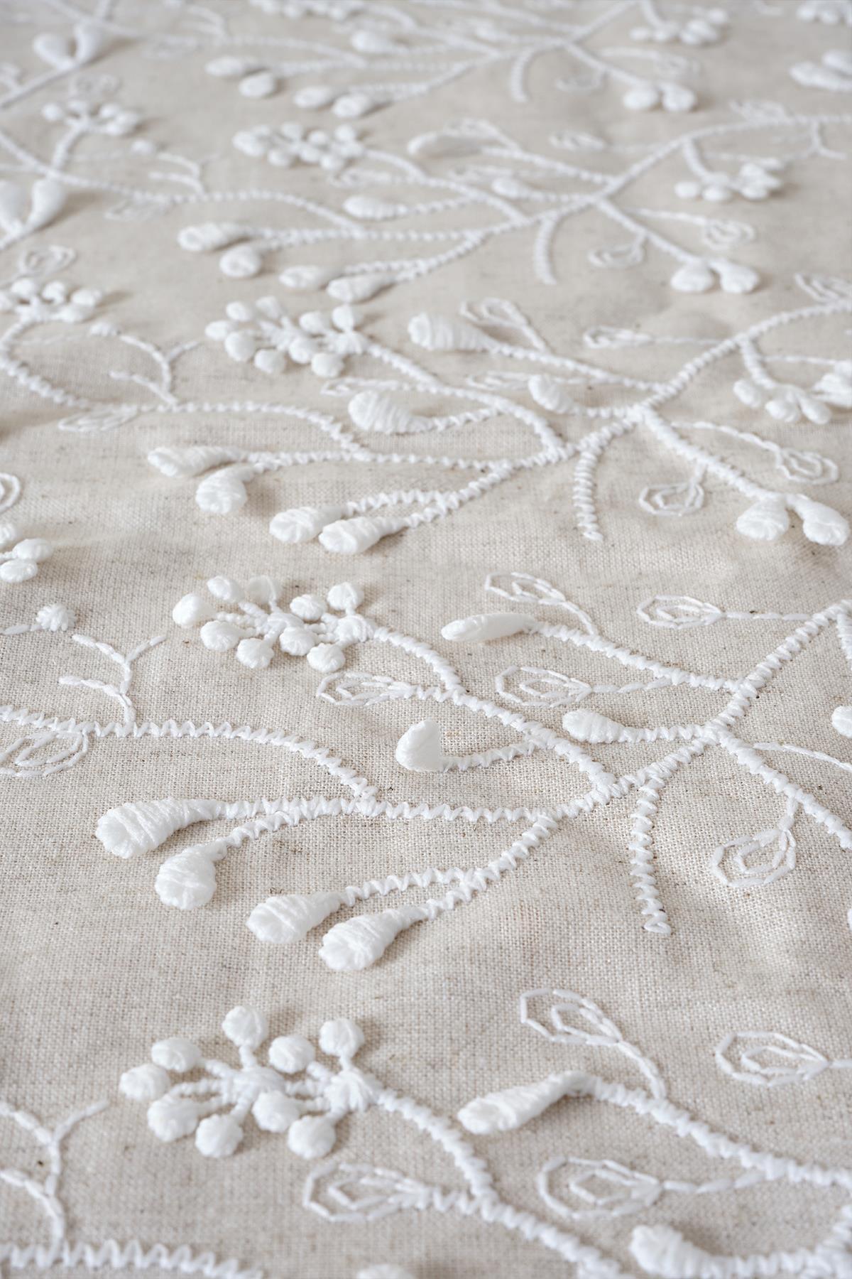 Primer plano de tela bordada con diseño de flores blancas en relieve sobre fondo beige