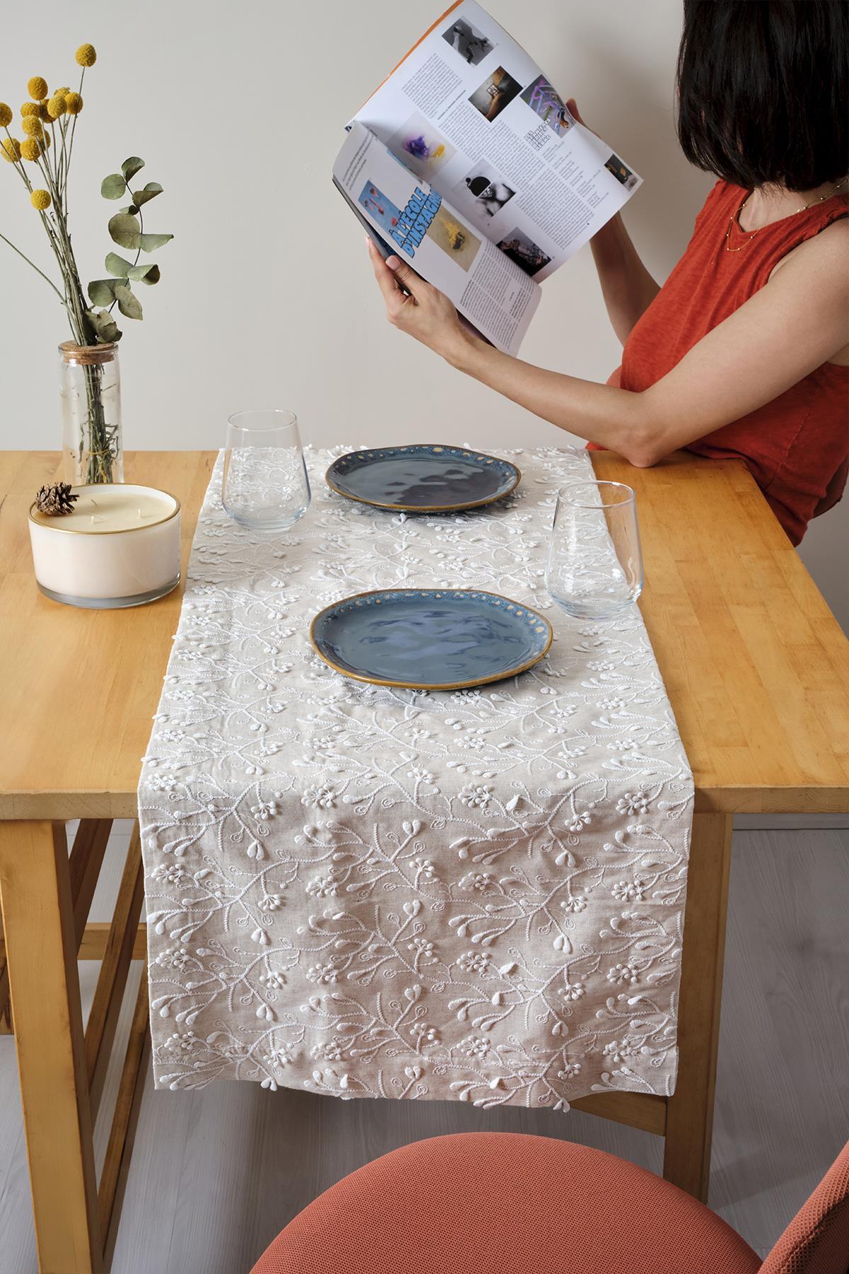 Camino de mesa de encaje crema sobre mesa de madera, dos platos azules y una elegante decoración de mesa.
