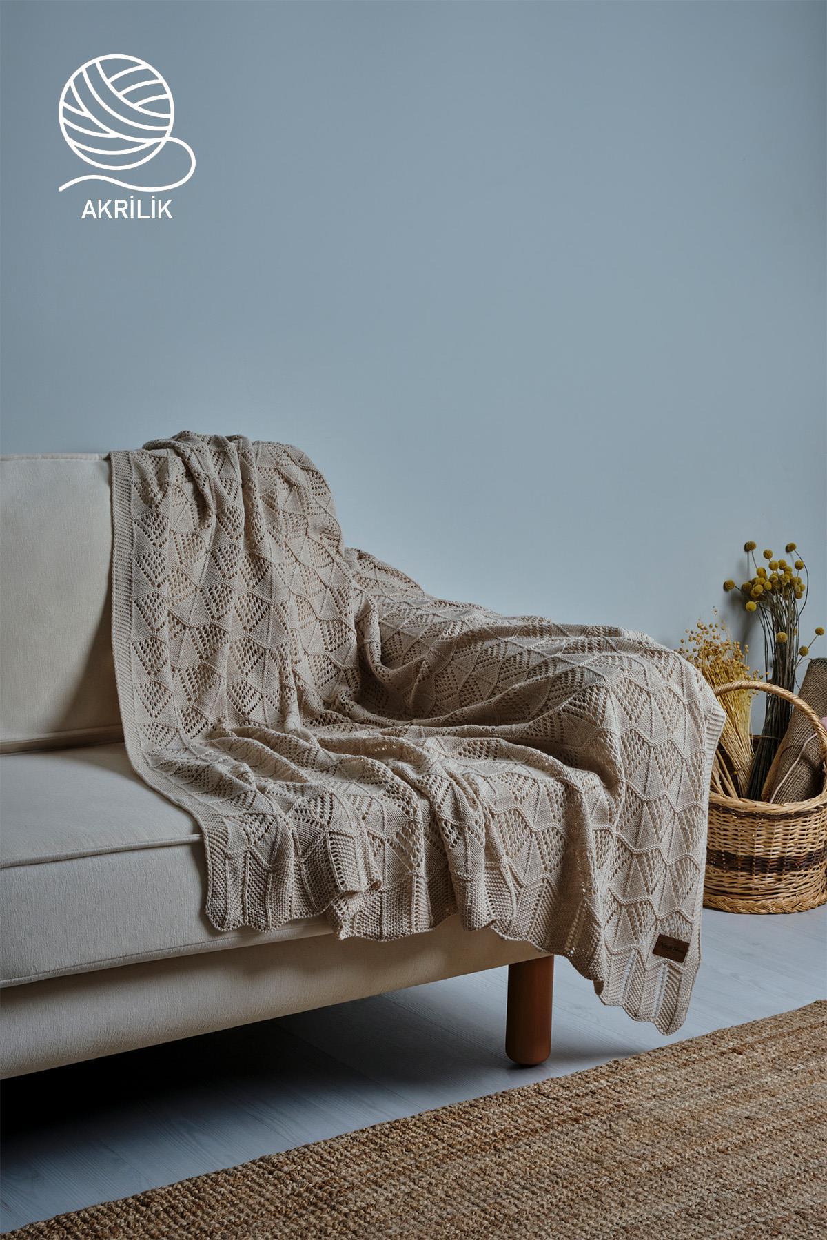 Manta de sofá de punto acrílico en color crema, extendida sobre un sofá en una habitación con decoración moderna