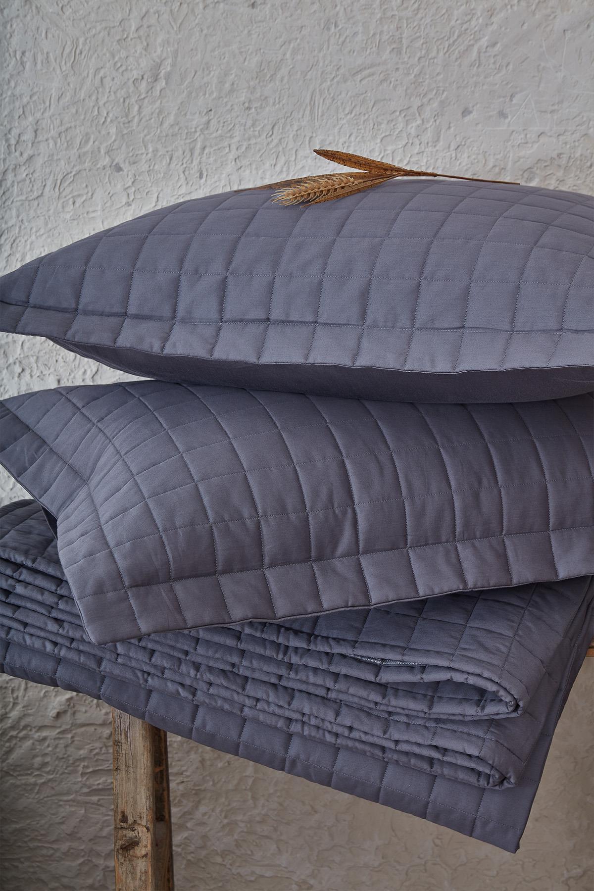Colcha doble gris acolchada con fundas de almohada, frente a una decoración natural