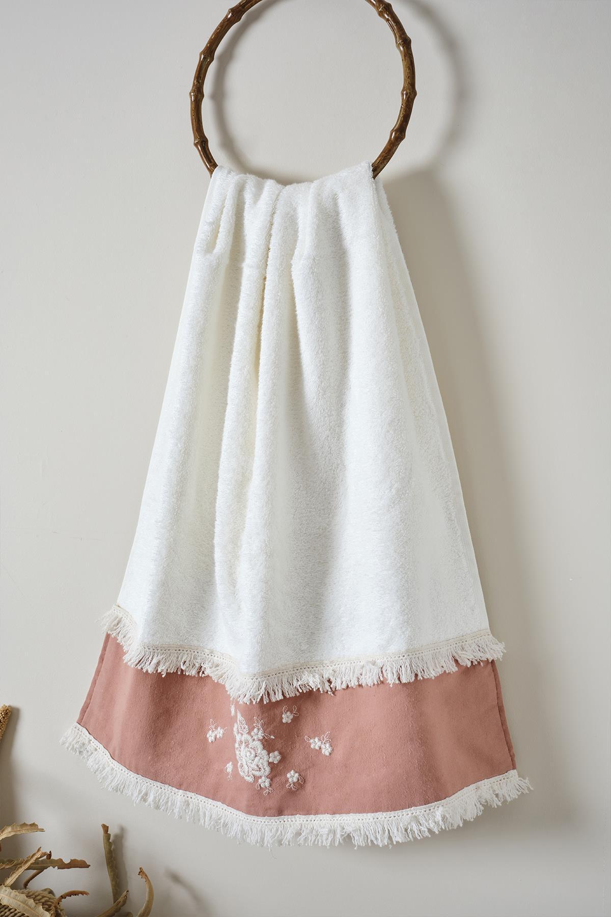 Toalla de baño blanca con encaje rosa y borlas, colgada en un perchero