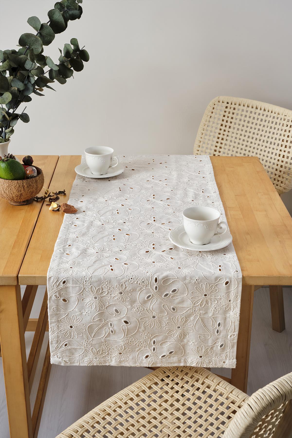 Camino de mesa color crema con bordado de encaje, presentación decorativa con dos tazas sobre una mesa de madera