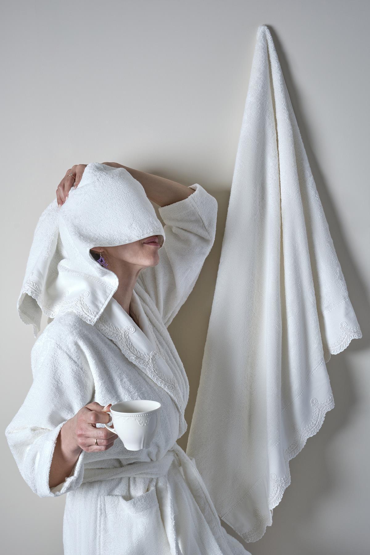 Mujer con albornoz de bambú blanco sosteniendo una taza y toalla colgada en la pared