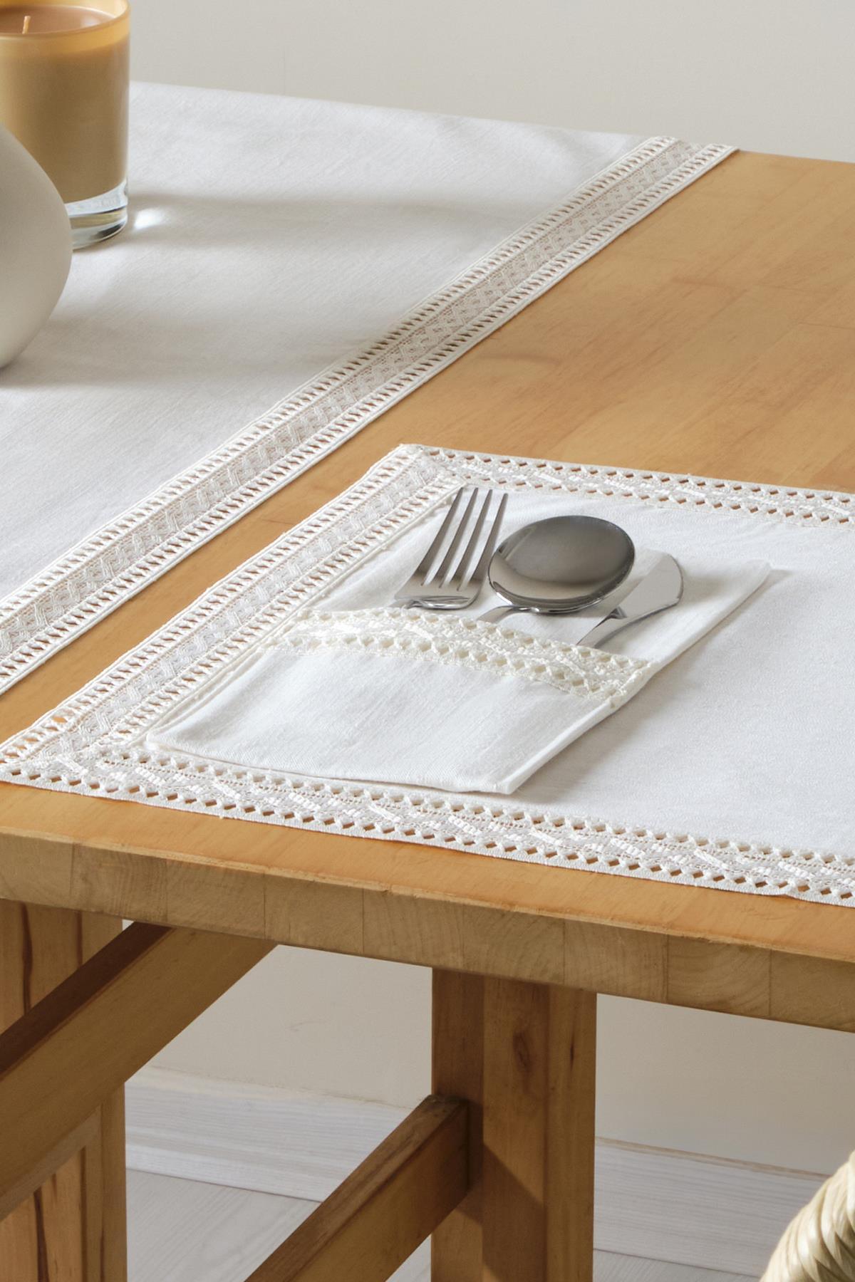 Mantel blanco de encaje y servilletero con tenedor, cuchara y cuchillo sobre una mesa de madera