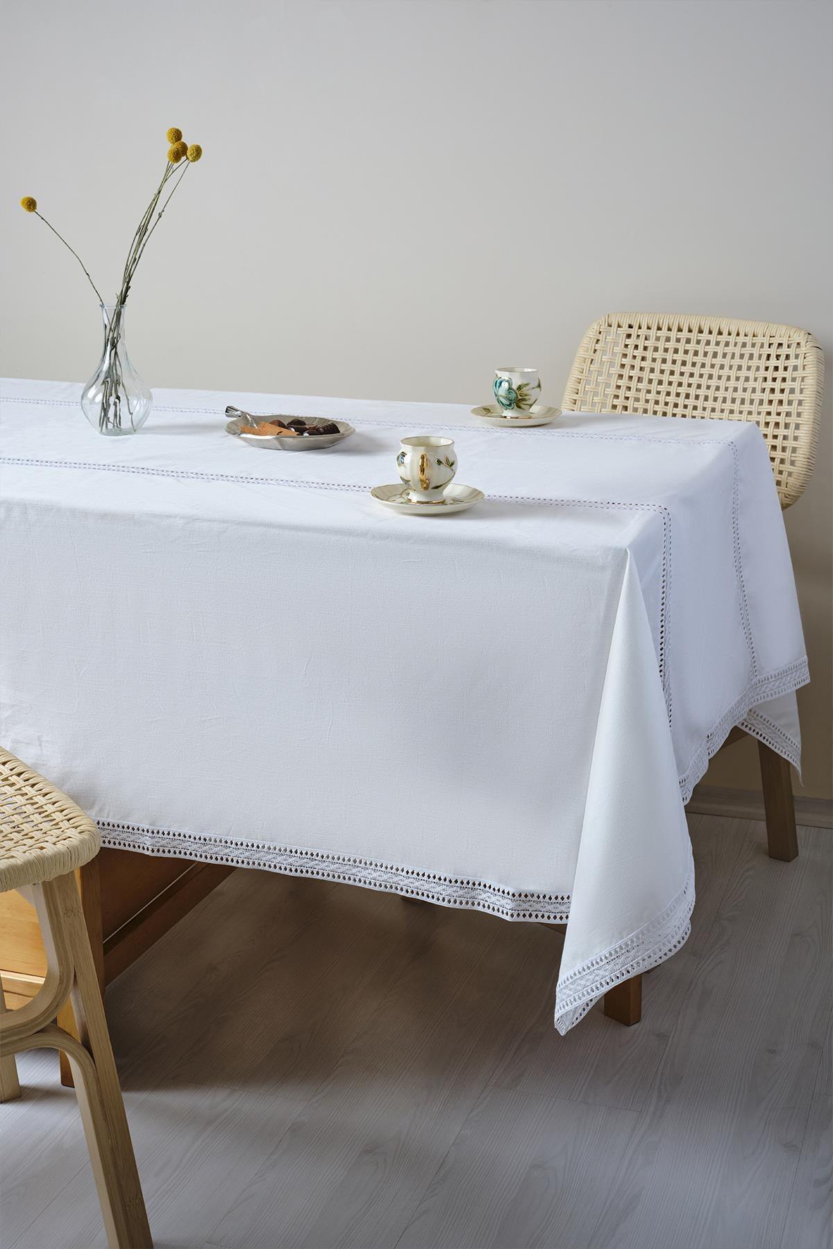 Mesa cubierta con un mantel blanco, con tazas de porcelana y un jarrón con flores encima.