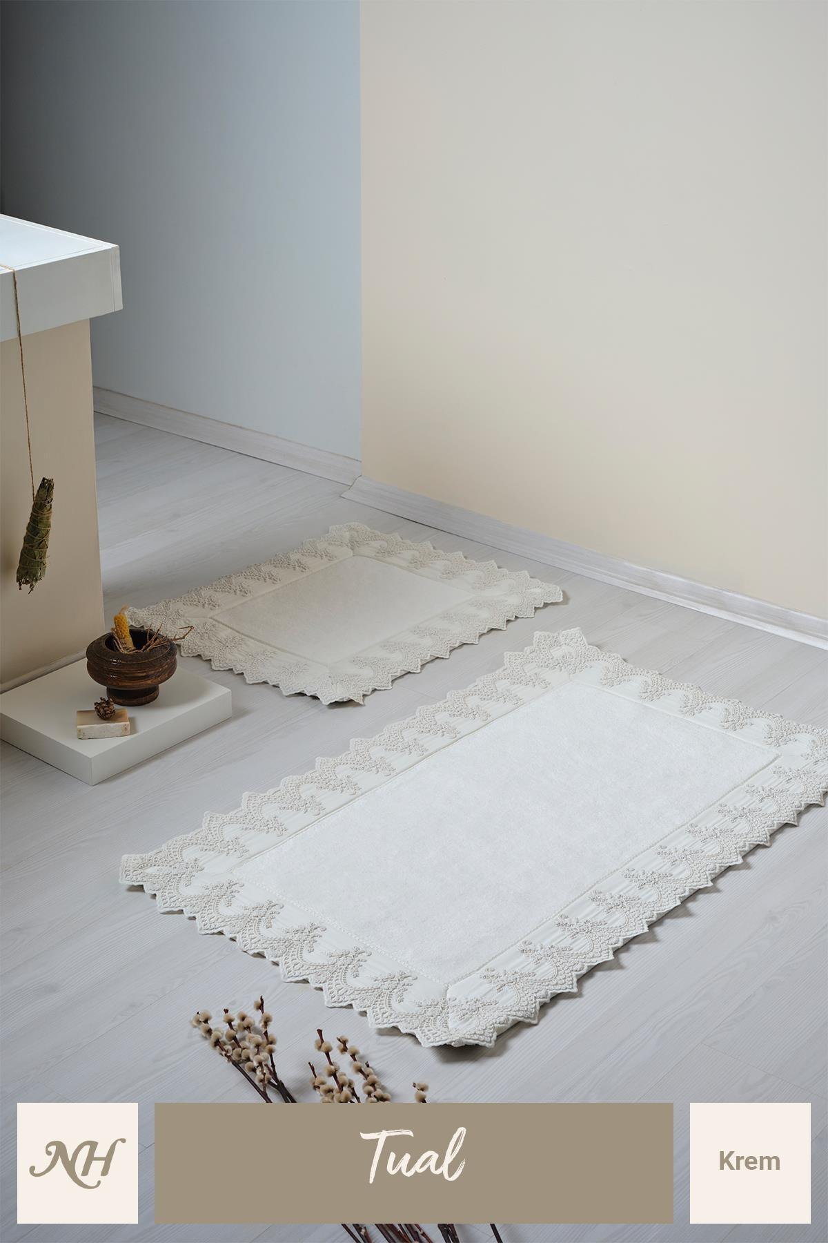 Juego de dos alfombrillas de baño color crema con detalles de encaje, sobre un suelo de baño moderno y elegante