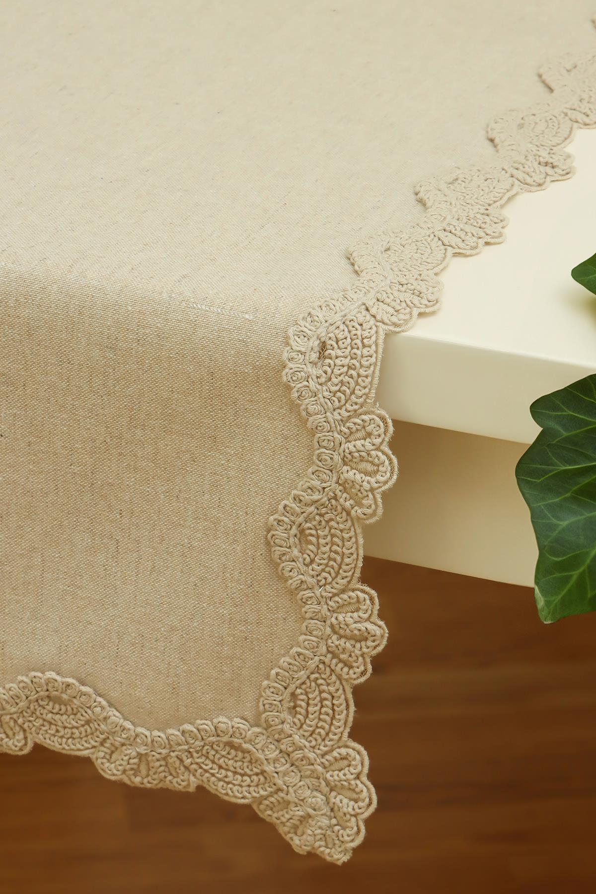Mantel de mesa color crema con borde de encaje sobre una mesa rectangular