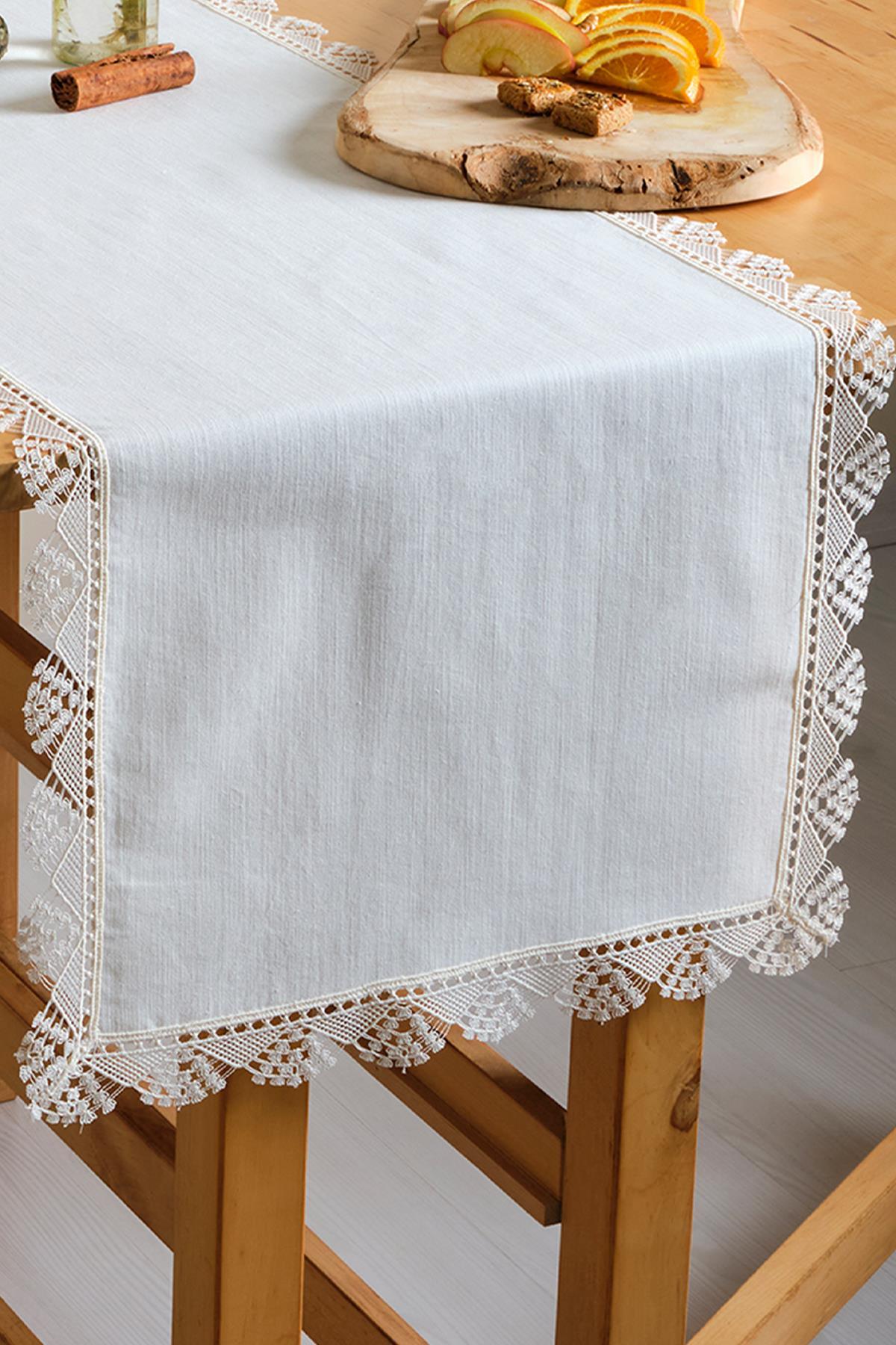 Camino de mesa blanco con encaje sobre una mesa de madera, decorado con frutas y galletas.